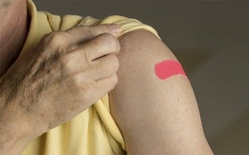 Senior holding up shirt sleeve to show bandaid after vaccination