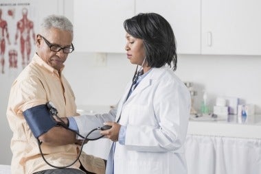 African American female doctor checking elder patient's blood pressure