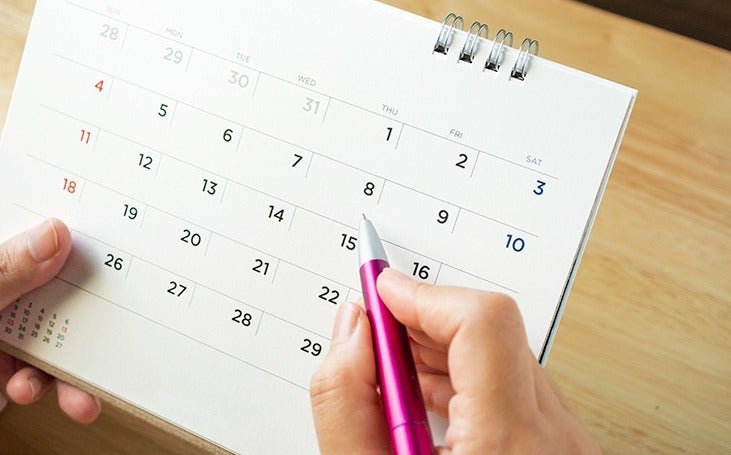 Calendar page with female hand holding pen on desk table