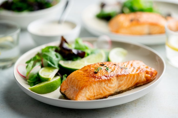 Grilled salmon on plate with salad and lime wedges